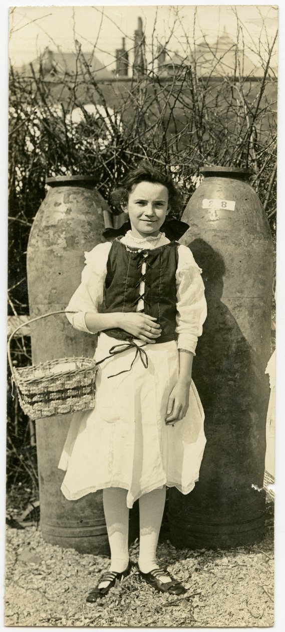 Photographie verticale sépia montrant une jeune fille en robe devant deux grandes obus d