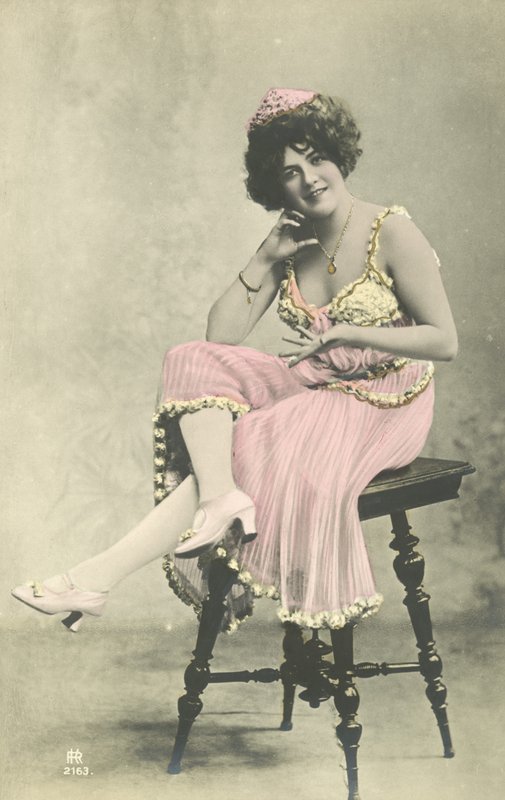 Actrice, avec un joli sourire, en robe rose assise sur un tabouret - French Photographer